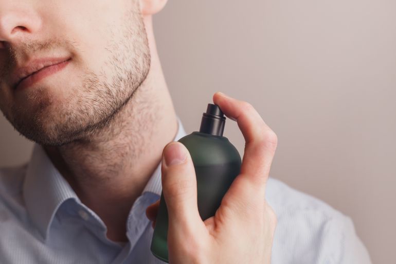 shutterstock_2105546858-1774608613 Handsome unshaven man applying perfume on neck, closeup. Pheromones and fragrance
