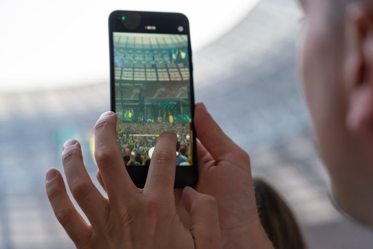 Hand of unidentified man records video with mobile smart phone of concert stage. Taking photo on front stage on summer outdoor music concert festival.