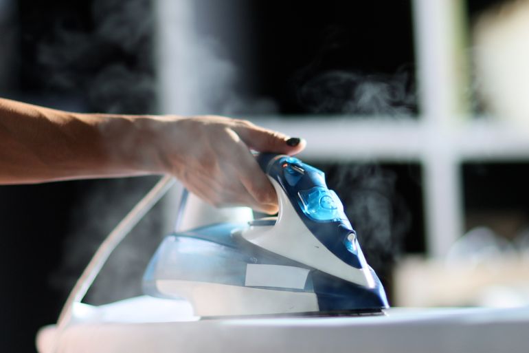 Selective focus of female hand irons white clothes with steam iron on an Ironing board. Push button of steam humidifier, laundry moistening function. Ironing linen using hot steam; Shutterstock ID 2269725747; purchase_order: aj; job: ; client: ; other:
