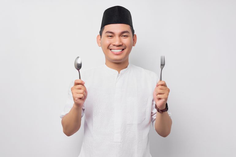 Smiling hungry young Asian Muslim man in Arabic clothes hold spoon and fork while prepare wait for delicious food to break fast isolated on white background. People religious Islamic lifestyle concept; Shutterstock ID 2271073951; purchase_order: aj; job: ; client: ; other: