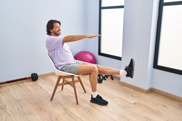 shutterstock_2300467745-1774263020 Middle age man smiling confident sitting on chair stretching at sport center