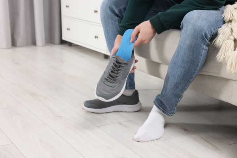 Man putting orthopedic insole into shoe indoors, closeup. Space for text