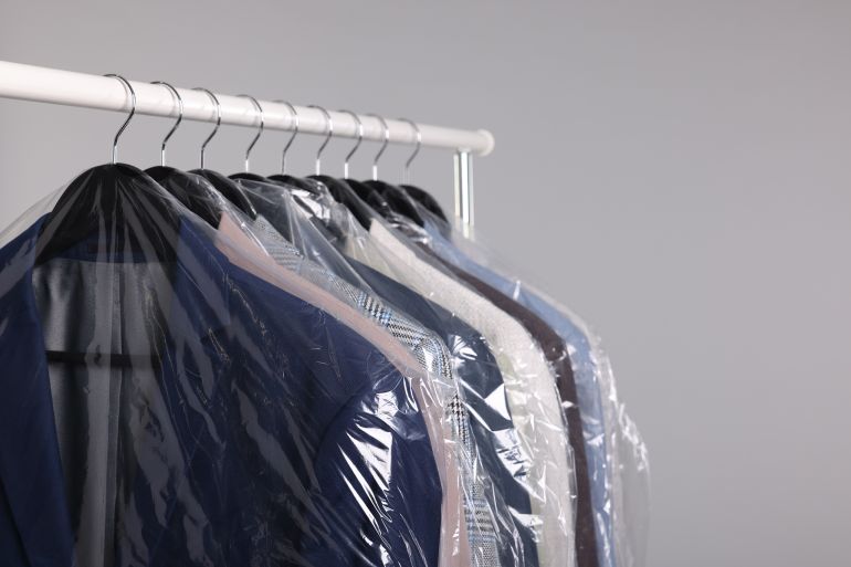 Dry-cleaning service. Many different clothes in plastic bags hanging on rack against grey background, space for text; Shutterstock ID 2416815711; purchase_order: aj; job: ; client: ; other: