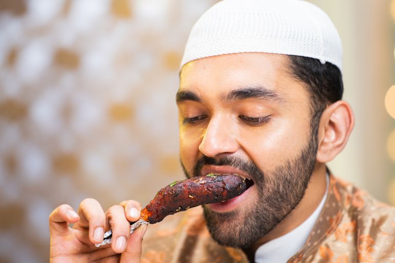 Close up head shot of muslim man eating chicken leg piece during ramadan festival feast; Shutterstock ID 2444126671; purchase_order: aj; job: ; client: ; other: