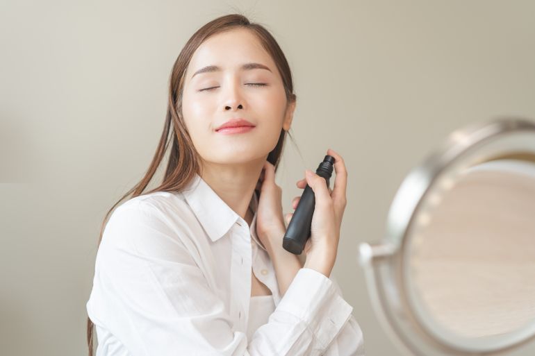 shutterstock_2466679003-1774608377 Perfume of essential aroma, beauty fashion concept. attractive perfect asian young woman hand holding perfume bottle, using spray and applying fragrance, scent at neck on body, isolated on background.