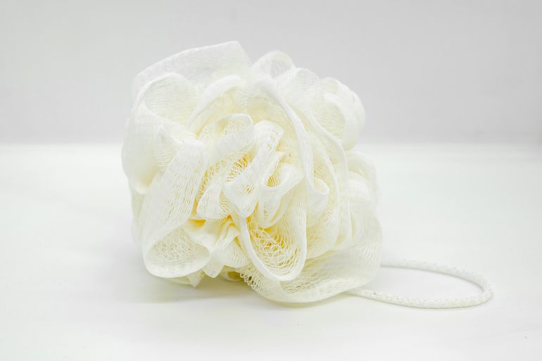Beige synthetic soft mesh pouf for body on white background. synthetic mesh washcloth for bath; Shutterstock ID 2564578061; purchase_order: aj; job: ; client: ; other: