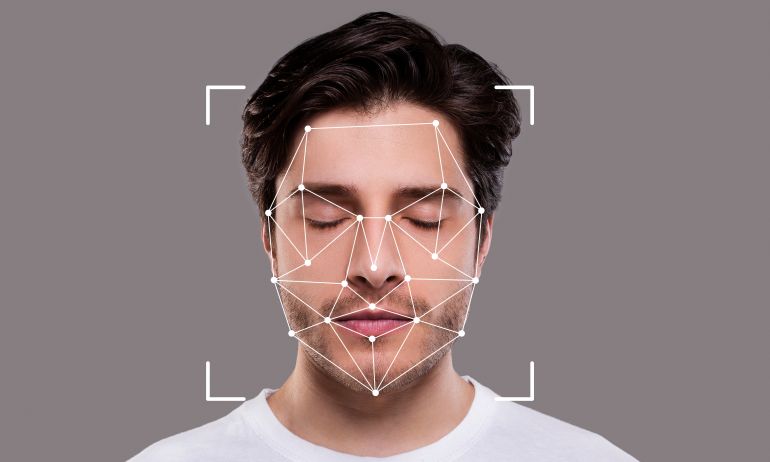 A person with closed eyes is engaged in facial recognition technology. An overlay of geometric shapes indicates the mapping of facial features for identification purposes.