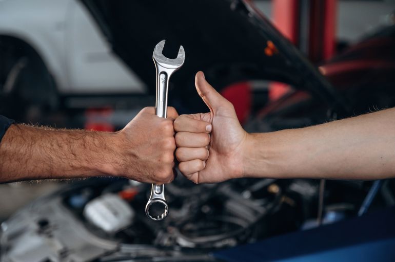 Hands of mechanic and client, holding tool, car service station.