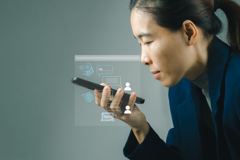 **داخلية** Business woman chatting with chatbot via mobile smart phone application while working on laptop computer. Chatbot assistant conversation, Ai Artificial Intelligence technology concept.