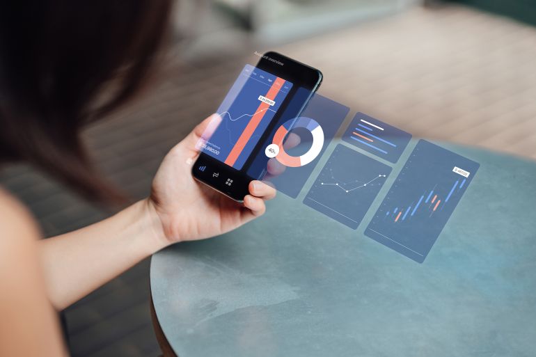 Closeup shot of young businesswoman analysing finance data on smartphone with virtual reality technology. Stock exchange market trading board in background. Blockchain concept. Crytocurrency market.
