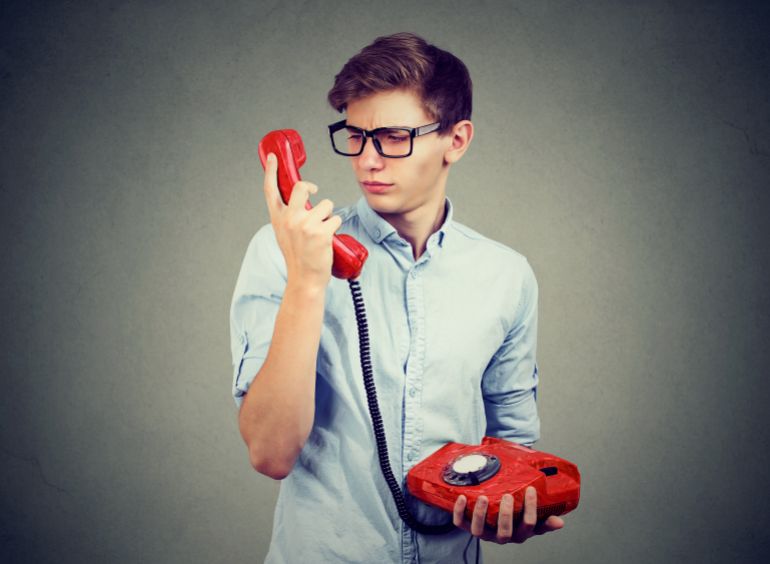 Confused worried teenager man looking at old fashioned telephone