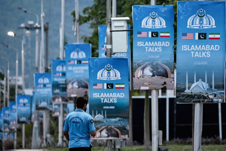 A police personnel walks past posters highlighting Pakistan's mediation of Iran–US peace talks, at the Red Zone area in Islamabad on April 18, 2026.
