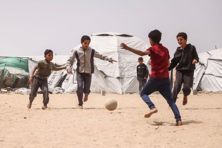 Children play football amid makeshift shelters for displaced Palestinians in Khan Yunis in the southern Gaza Strip on April 18, 2026.