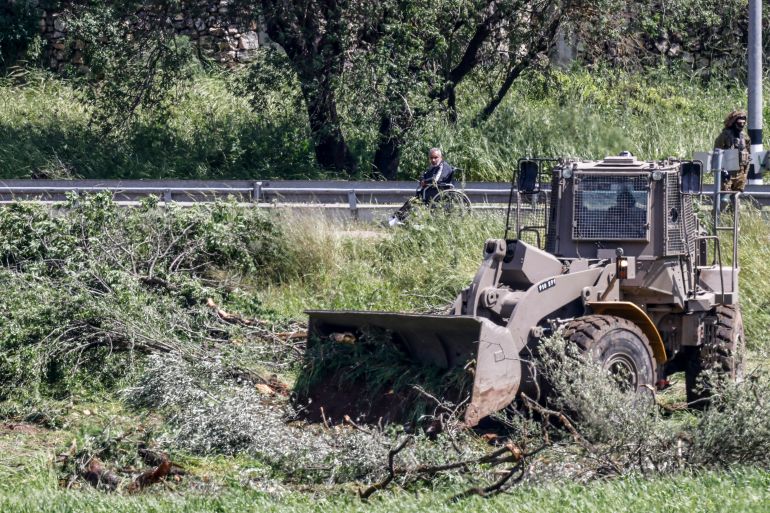 A Palestinian man looks on while Israeli soldiers stand guard as a bulldozer uproots olive trees in a field belonging to Palestinians on the outskirts of the village of Al-Lubban ash-Sharqiya, south of Nablus in the occupied west bank, on April 20, 2026. (Photo by Zain JAAFAR / AFP)