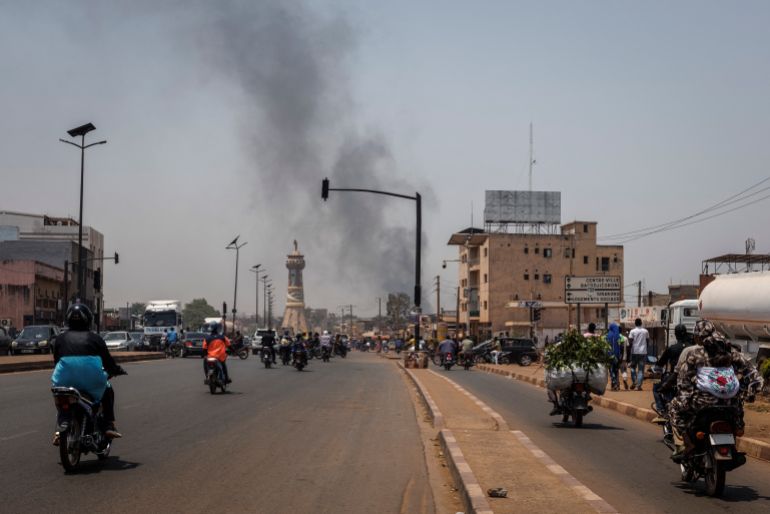 A column of black smoke rises above buildings as traffic passes the Africa Tower monument in Bamako on April 26, 2026.