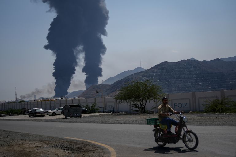 FILE - A man rides a bike as fires and plumes of smoke rise after debris from an intercepted Iranian drone struck an oil facility, according to authorities, in Fujairah, United Arab Emirates, March 14, 2026. (AP Photo/Altaf Qadri, File)