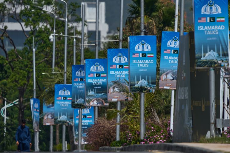 A worker walks past billboards of U.S. and Iran talks near the Serena Hotel in Islamabad, Pakistan, Wednesday, April 22, 2026. (AP Photo/Anjum Naveed)