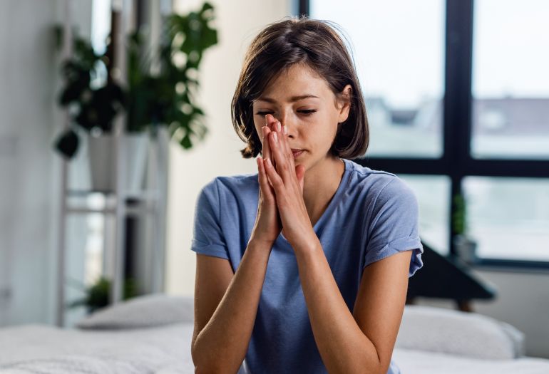 Young thoughtful woman alone sitting on the bed.