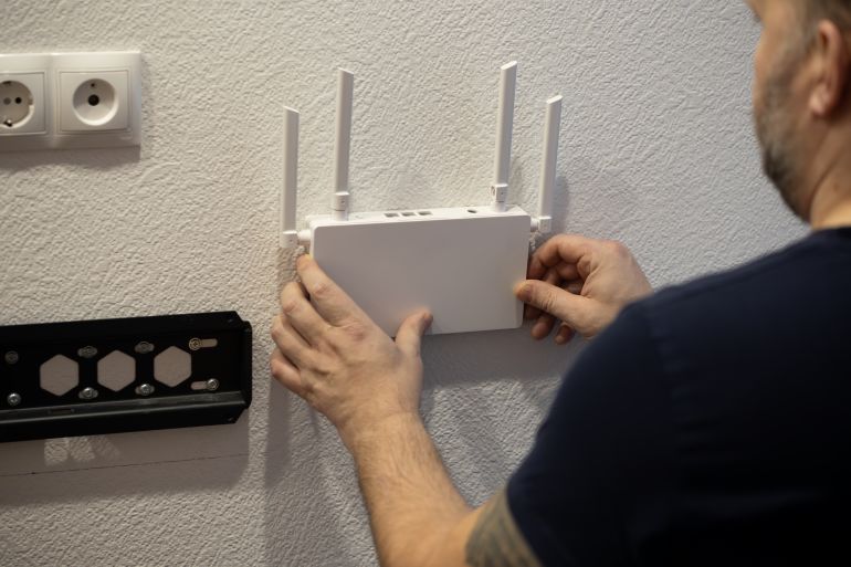 A man is carefully mounting a wireless router onto a wall in a sleek and modern interior space of the home