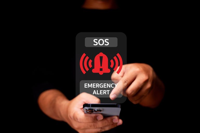 A person activates an emergency alert on a smartphone, displaying an SOS warning with red alert icons on a dark background.