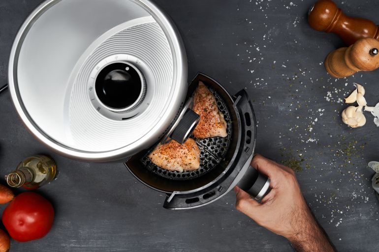 Unrecognizable man hand cooking skinless chicken breast with spices in an air fryer by Francisco Zeledon @ ادوبي ستوك