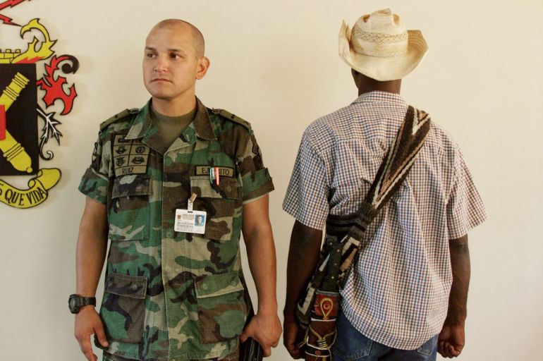 getty_69f15e8fde-1777426063 PATILLAL, COLOMBIA - AUGUST 23: Mayor Jose Ruiz, in charge of intelligence gathering at La Popa military base, posses accompanied with an unidentified informer August 23, 2002 in Valledupar, Colombia. Part of the new strategies of Colombian president Alvaro Uribe Velez to combat guerrilla groups through out the country is to hire thousands of informers who will inform against terrorist plots or ambushes against the armed forces before they became a reality. Velez's administration has told the nation's highest court Colombian rebels are planning devastating attacks with sophisticated weapons, therefore justifying Velez's assumption of special powers. (Photo by Carlos Villalon/Getty Images)