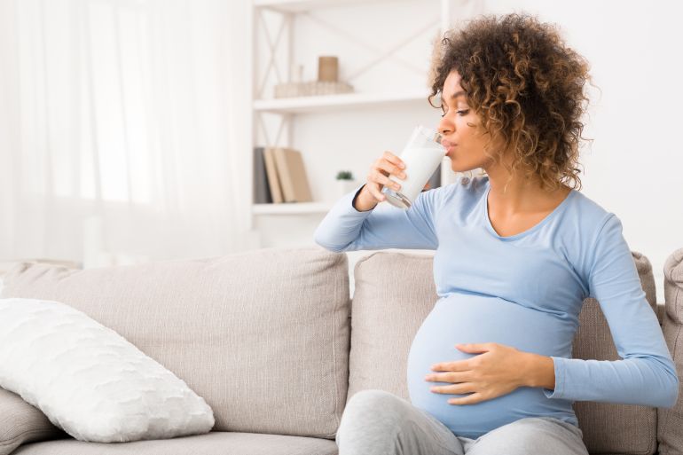 gettyimages-1183113709-1728748541 Nutrition and vitamins. Pregnant woman drinking glass of milk, enjoying healthy drink