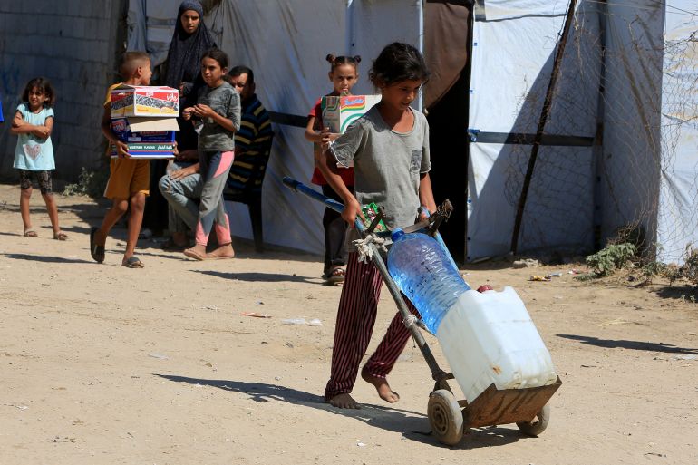DEIR AL-BALAH, GAZA - AUGUST 15: Palestinian children, who had to migrate to the city to protect themselves from the Israeli attacks, carry bottles, filled with clean water, distributed by aid organizations, in Deir al-Balah, Gaza on August 15, 2024. (Photo by Abed Rahim Khatib/Anadolu via Getty Images)