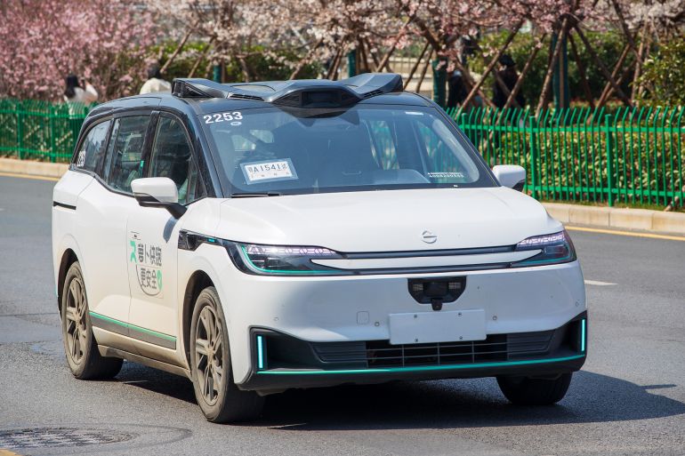 WUHAN, CHINA - MARCH 10: A robotaxi launched by autonomous ride-hailing platform Apollo Go runs past blooming cherry blossoms along the street on March 10, 2026 in Wuhan, Hubei Province of China. (Photo by Ji Pengfei/VCG via Getty Images)