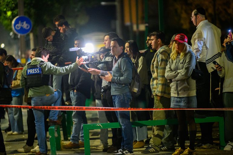TEL AVIV, ISRAEL - MARCH 27: Members of the media, and bystanders, including one wearing a "Make America Great Again" hat watch first responders and security services responding to the scene where one person was killed from shrapnel following an Iranian Ballistic cluster munitions missile strike on March 27, 2026 in Tel Aviv, Israel. Iran has continued firing waves of drones and missiles at Israel after the United States and Israel launched a joint attack on Iran early on February 28th. (Photo by Alexi Rosenfeld/Getty Images)
