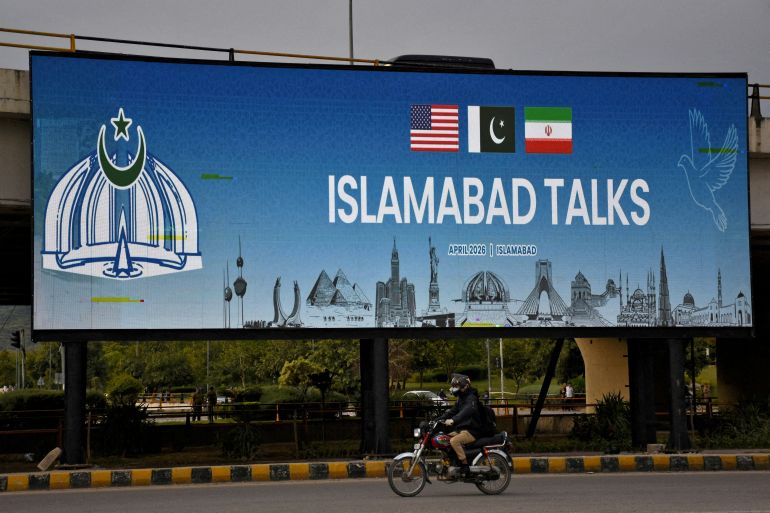 FILE PHOTO: A man rides his motorbike past a billboard installed alongside a road as Pakistan prepares to host the U.S. and Iran for peace talks, in Islamabad, Pakistan, April 10, 2026. REUTERS/Waseem Khan/File Photo