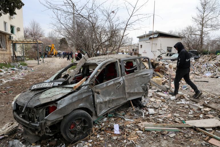 A man walks past a destroyed car at the scene following an overnight explosion at a multi-storey residential building in Sevastopol, Crimea, March 24, 2026. REUTERS/Alexey Pavlishak