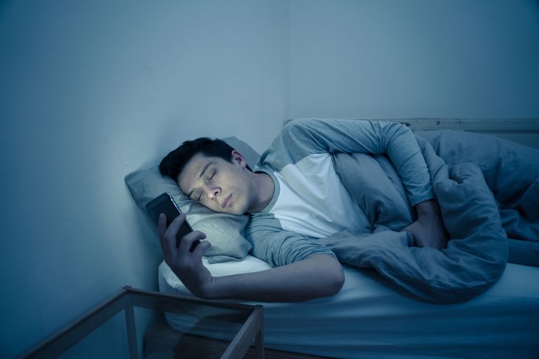 Addicted man chatting and surfing on the Internet with smart phone late at night in bed. Bored, sleepless and tired in dark room with moody light. In insomnia and mobile addiction concept.