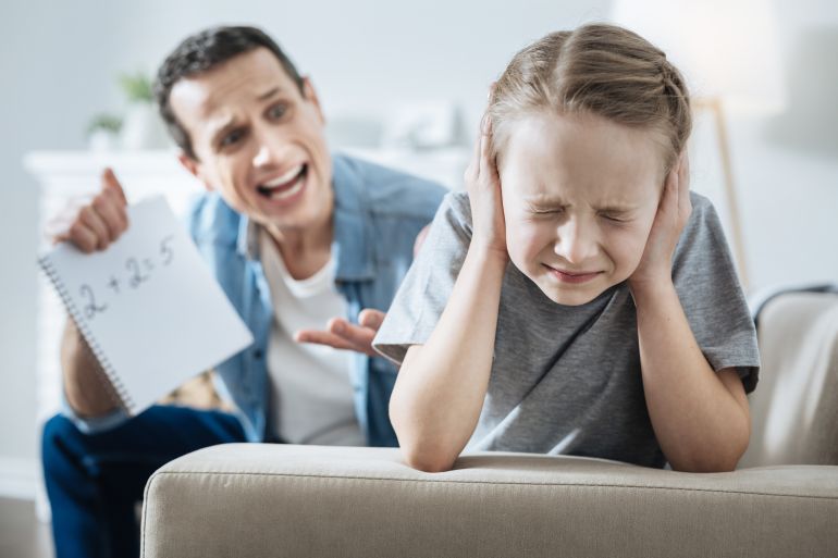 Stupid. Outraged dark-haired young father holding and pointing at his daughters incorrect equation and shouting at her