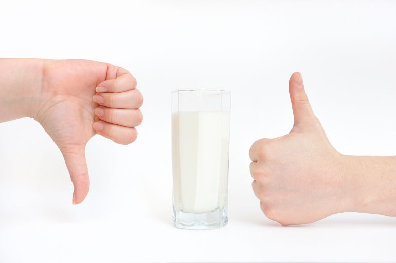 A glass of milk and hands close-up show a sign - like and dislike. Milk is useful and not useful, harmful and not harmful