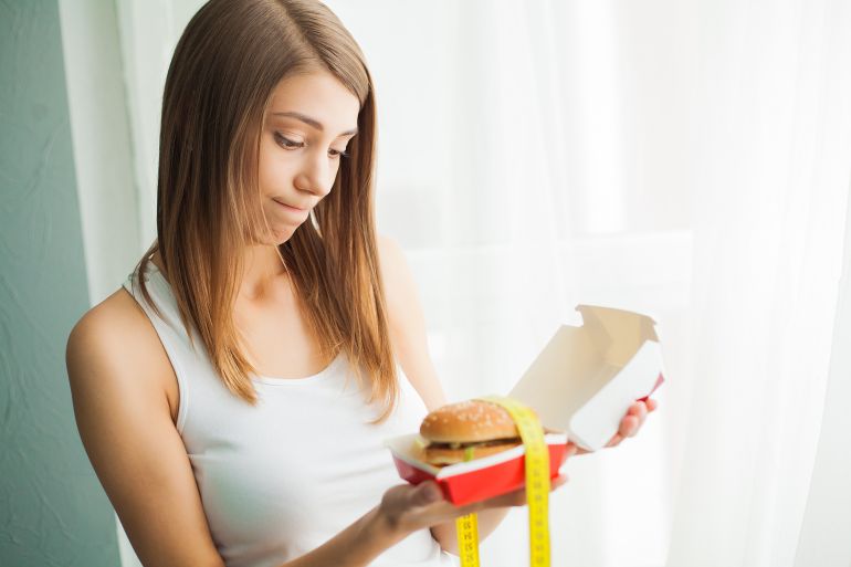 Diet. Woman with guilty feeling to eat a hamburger.