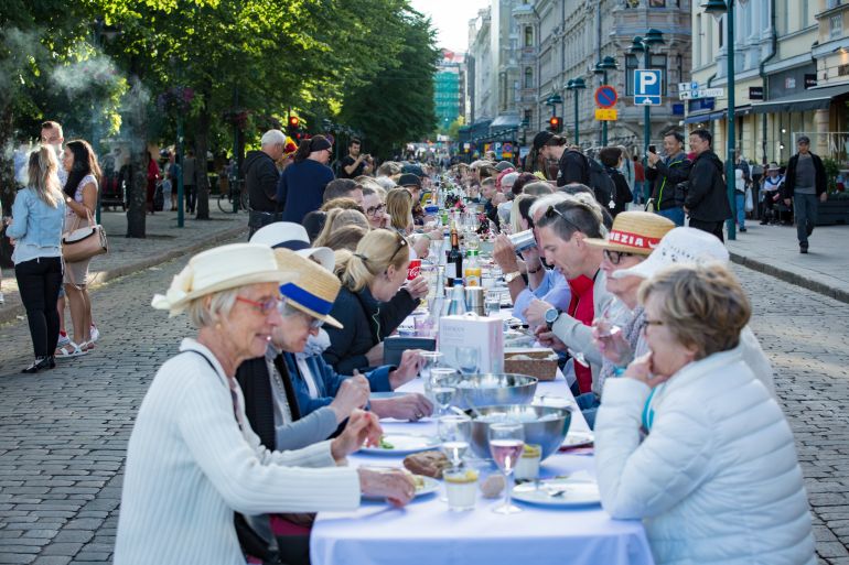 Helsinki, FINLAND - JUNE 12, 2018: Long table with lots of people eating and drinking together. The Day of City Celebration in centre of Helsinki. Finnish your dinner under the sky.