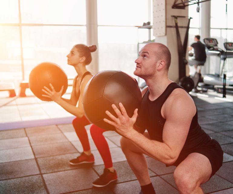 Сouple functional training. Sporty man and fit woman do exercise with medicine ball in gym