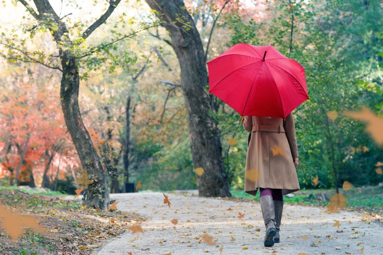 woman with red umbrella walking at the rain in beautiful autumn park, back view with copy space