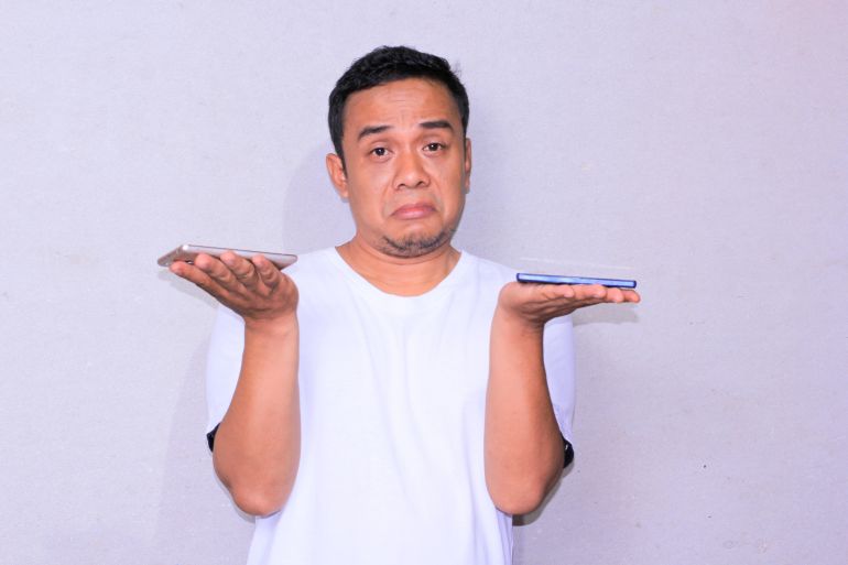 young Asian man expression confuse choose two phone between of his hands.