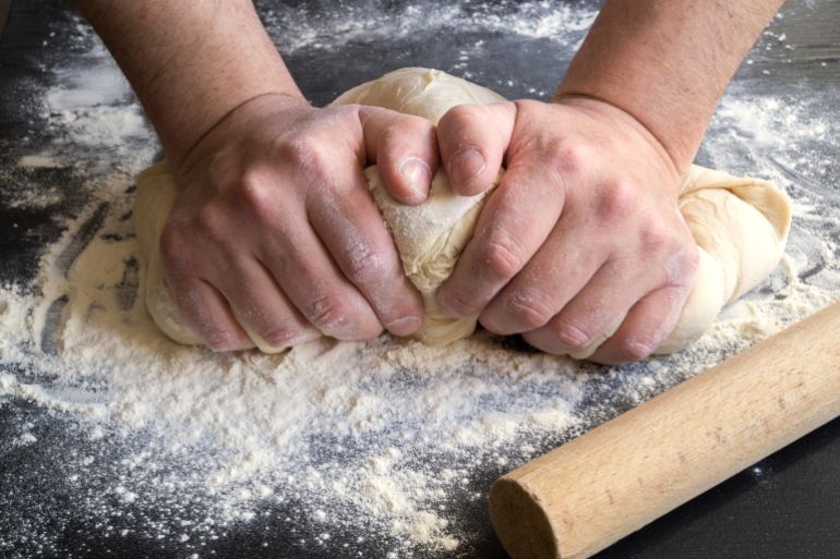 men's hands knead dough on a floured table.