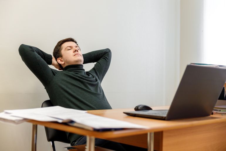 Relaxed corporate man sitting with closed eyes contemplating at work desk with laptop in office. Guy relaxing, relieves stress, gets positive thinking with yoga exercise. Stress free workplace concept