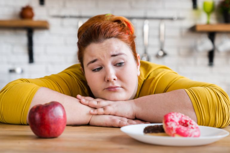 Sad plump fat woman choosing between sweets and fruits, healthy eating and junk food. The choice. Two options. The choice between eating. Delema, for a healthy lifestyle or not.
