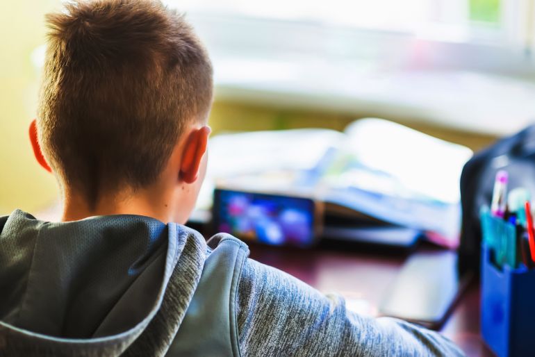 Distance learning online education. A schoolboy 10s boy studies at home and does school homework.Child sitting at table with smart phone,does remote homework.Selective soft focus blurred background.