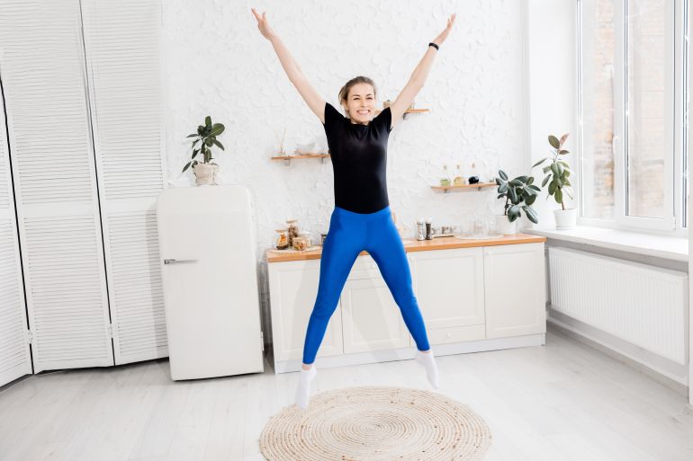 Brunete-hair stylish female is warming up before workout at home, jumping. Athletic young woman doing exercise, smiling, motivate to healthy lifestyle, morning training concept. High quality photo