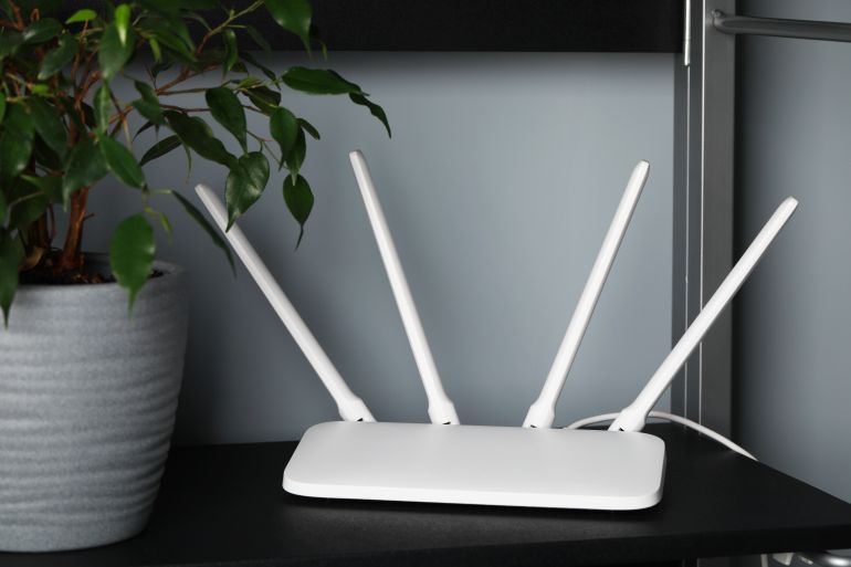 New white Wi-Fi router near potted plant on black shelf