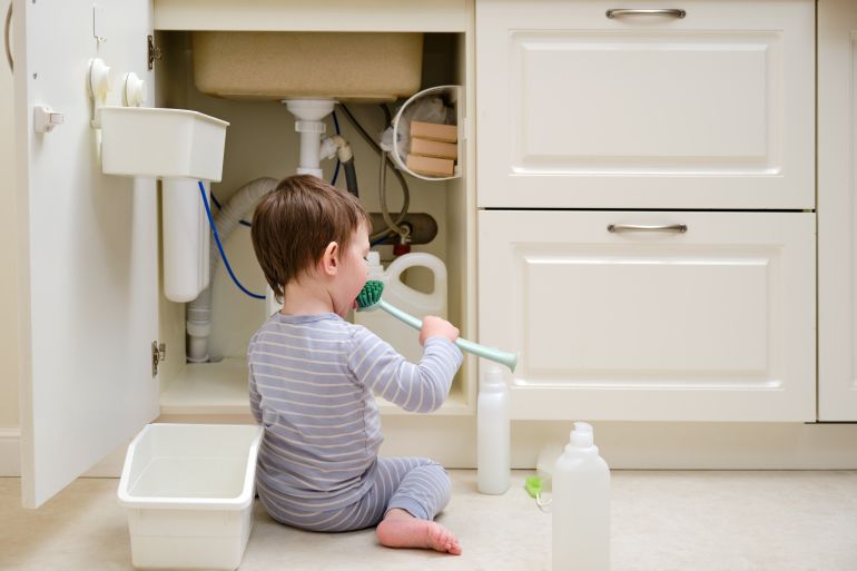 A child is playing with chemical cleaning products under the sink in the kitchen. Baby holds bottles with detergent. Kid aged about two years (one year nine months)
