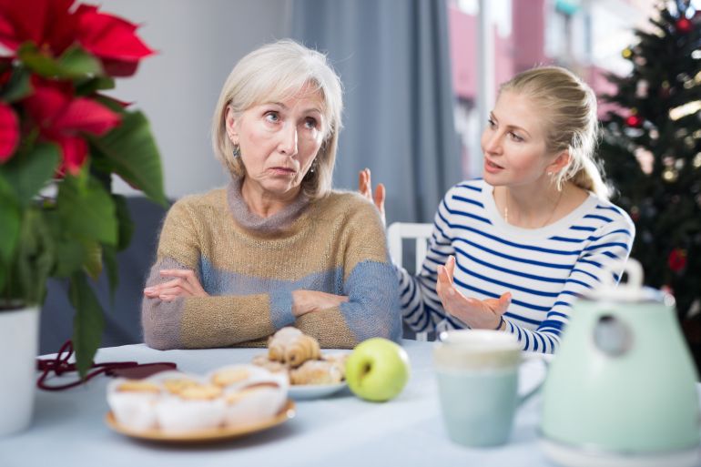 Adult daughter explains something to a mature dissatisfied mother, sitting at the table