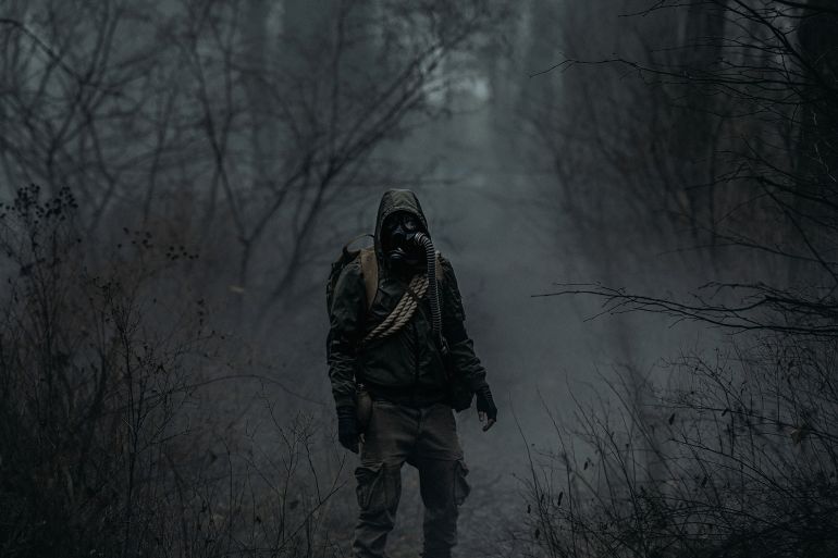A man in camouflage in a post-apocalyptic smoky dark forest. Front view. The concept of a lone survivor after a nuclear disaster or war.