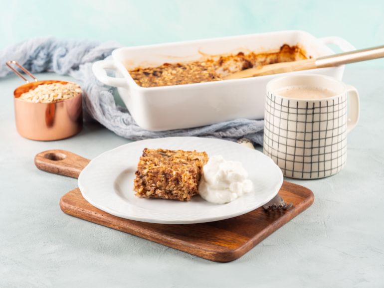 Baked oatmeal peanut butter porridge with chocolate chips served on white plate with greek yogurt. Healthy breakfast bars and mug of latte coffee